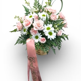 Pink roses and white daisies in a basket with a pink ribbon
