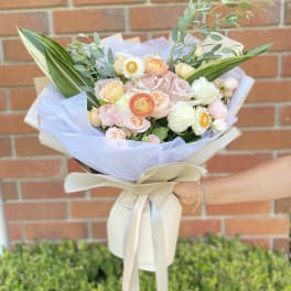 Hand-tied bouquet of pastel roses and white daisies wrapped in pale paper