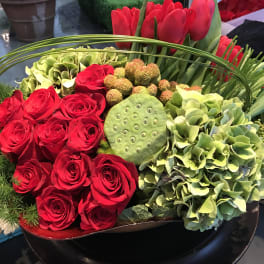 Red roses and green hydrangeas arranged in a black bowl with lotus pods