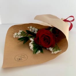Single red rose wrapped in brown paper with white filler flowers