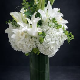 White lilies and hydrangeas arranged in a clear glass vase