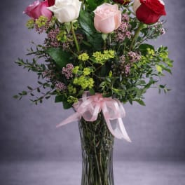 Mixed roses in a tall glass vase with a pink ribbon
