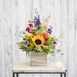 Colorful mixed flower arrangement in a wooden box with a candle beside it