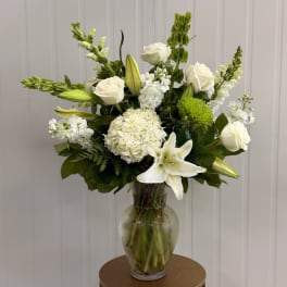 White roses and lilies arranged in a glass vase with green accents