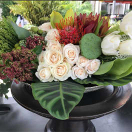 Mixed floral arrangement with cream roses, white tulips, and green tropical accents in a black pedestal bowl