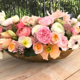 Low floral arrangement of pink and peach blooms in a gold bowl