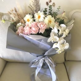 Bouquet of pink roses, white flowers, and dried grasses wrapped in gray paper