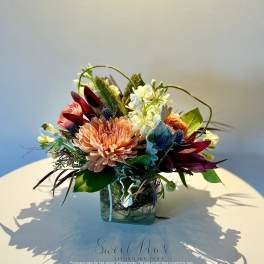 Mixed floral arrangement in a square glass vase with peach and burgundy blooms