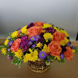 Basket arrangement of orange roses, yellow daisies, and purple flowers