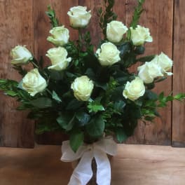 White roses arranged in a glass vase with a white ribbon