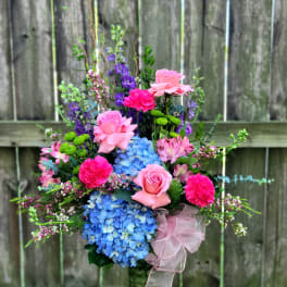 Pink and blue floral arrangement in a glass vase with a ribbon bow