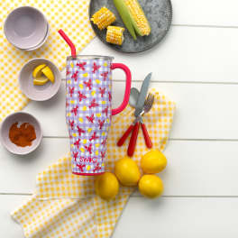 Patterned insulated tumbler with straw surrounded by lemons and picnic dishes