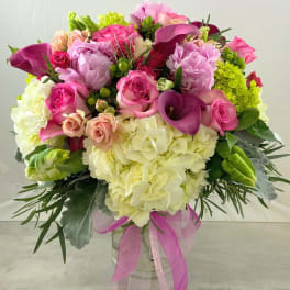Pink and white mixed bouquet in a clear glass vase with a pink ribbon