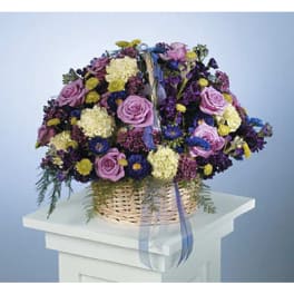 Lavender and purple mixed flower basket with cream blooms and ribbon on a white pedestal.