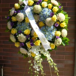 Standing funeral wreath with yellow roses, blue hydrangeas, and purple flowers