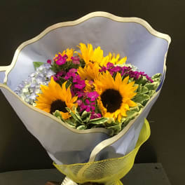 Bouquet of sunflowers and small purple flowers wrapped in pale paper