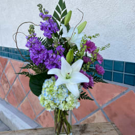 Purple flowers and white lilies arranged in a clear glass vase