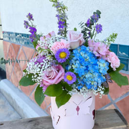 Bouquet of pink roses, blue hydrangeas, and purple flowers in a pink butterfly box