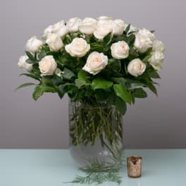 White roses arranged in a clear glass vase with greenery.