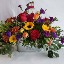 Mixed bouquet in a metal container with roses, sunflowers, and purple blooms