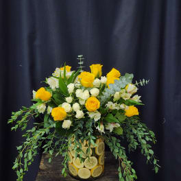 Yellow roses and white spray roses in a lemon-filled glass vase
