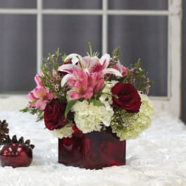 Bouquet of pink lilies, red roses, and white hydrangeas in a red glass vase