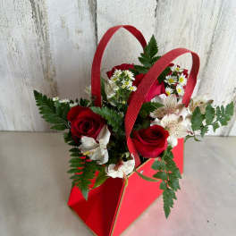 Red roses and white flowers in a red handled gift bag