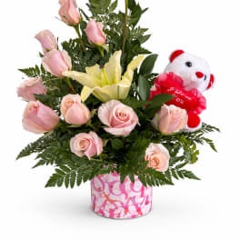 Pink roses and a yellow lily in a pink patterned vase with a teddy bear