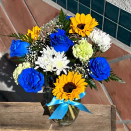 Bouquet of blue roses, sunflowers, and white daisies in a glass vase