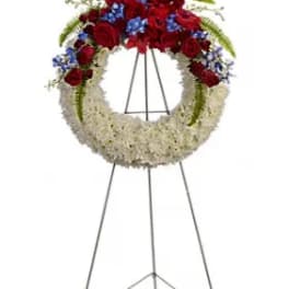 Circular funeral wreath of red and white flowers on a metal stand