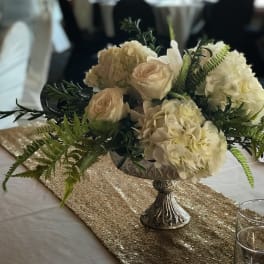 Cream floral centerpiece in a silver pedestal bowl on a table runner