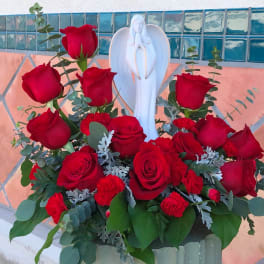 Red roses arranged around a white angel figurine in a vase
