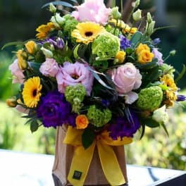 Mixed bouquet of pink, yellow, and purple flowers in a wrapped container