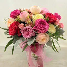 Pink and cream rose bouquet in a glass vase with a pink ribbon