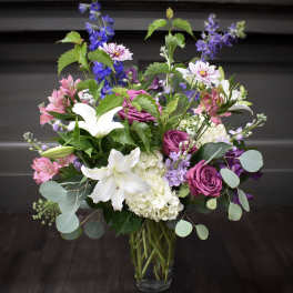 Mixed bouquet of white lilies, purple roses, and pink flowers in a glass vase