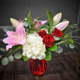 Pink lilies, red roses, and white hydrangea in a red vase