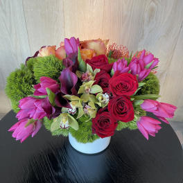 Pink tulips, red roses, and orchids arranged in a white vase