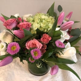 Pink tulips, roses, and white blooms arranged in a glass vase