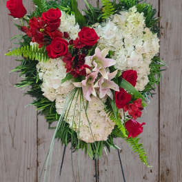 Heart-shaped floral wreath with red roses and white blooms on a stand