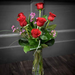 Red roses with small purple filler flowers in a clear glass vase