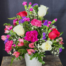 Mixed bouquet of roses, carnations, and purple filler in a white vase