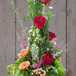 Tall floral arrangement with red roses, peach daisies, and pink berries in a vase