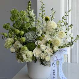 White and green floral arrangement in a white hatbox with a ribbon
