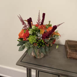 Orange and burgundy floral arrangement in a textured vase