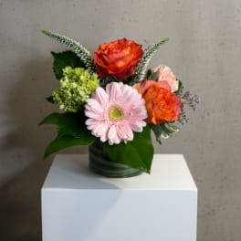 Small bouquet of orange roses and a pink gerbera daisy in a glass vase