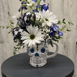 White daisies and blue flowers arranged in a skull mug with a black-and-white ribbon