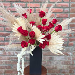 Red roses arranged with cream dried palm leaves in a black vase