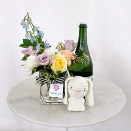 Mixed pastel roses in a glass vase with a plush bunny and bottle