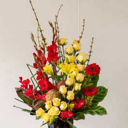 Tall bouquet of yellow roses, red flowers, and lilies in a black vase