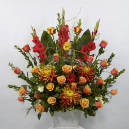 Tall arrangement of red and orange flowers in a white container